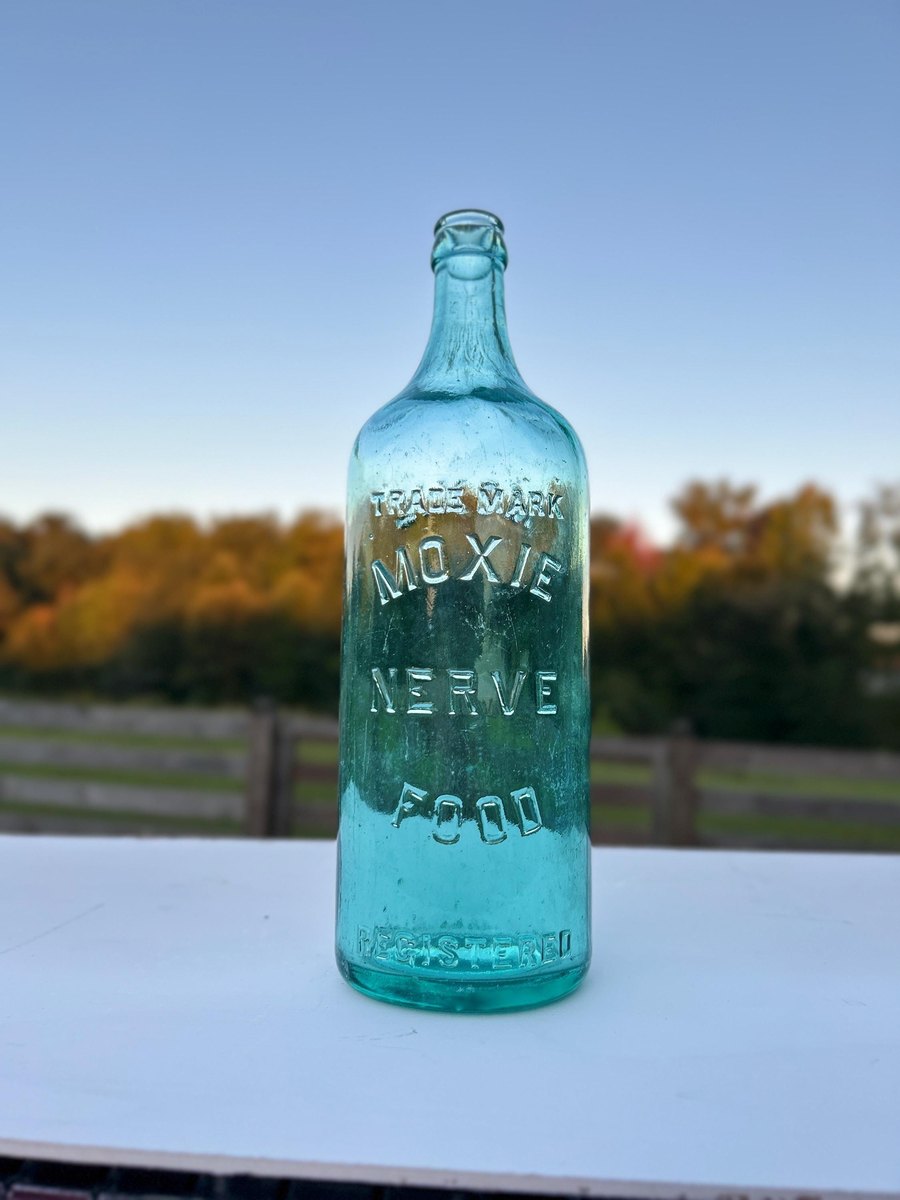 Antique Moxie Nerve Food aqua glass bottle with embossed lettering, photographed at dusk