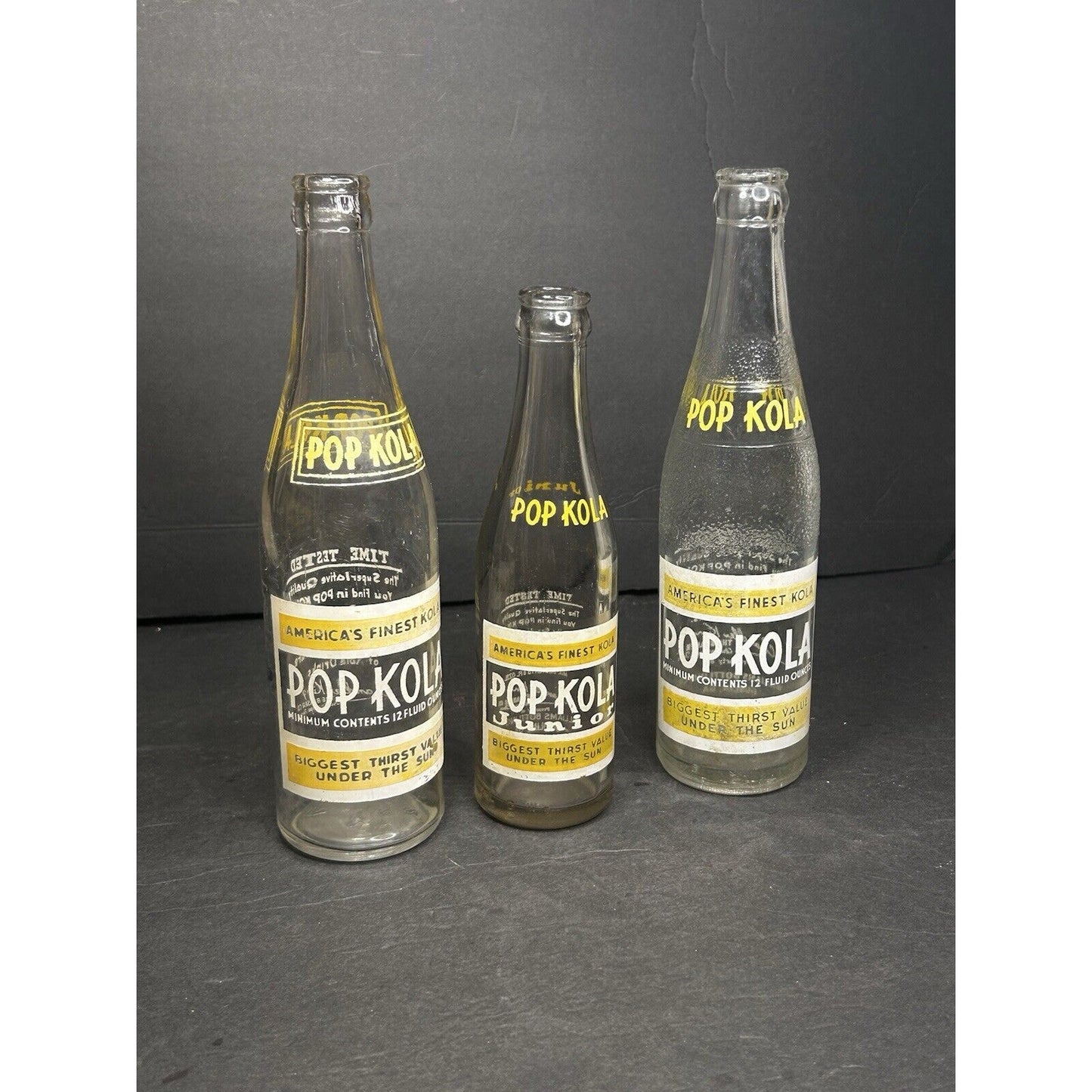 1930s Pop Kola soda bottle set back view — embossed glass body, vintage American soda advertising