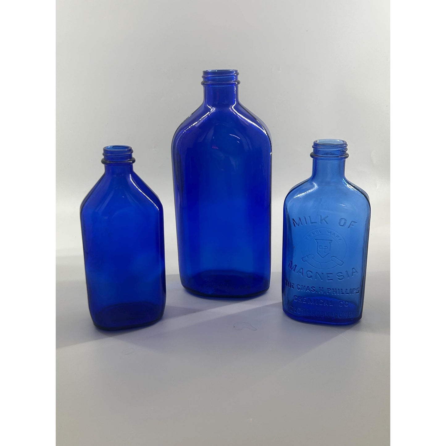 Phillips Milk of Magnesia antique blue bottle with larger companion cobalt pharmacy bottles — embossed apothecary glass