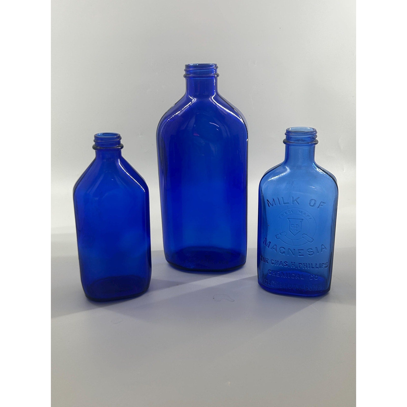 Phillips Milk of Magnesia antique blue bottle with larger companion cobalt pharmacy bottles — embossed apothecary glass