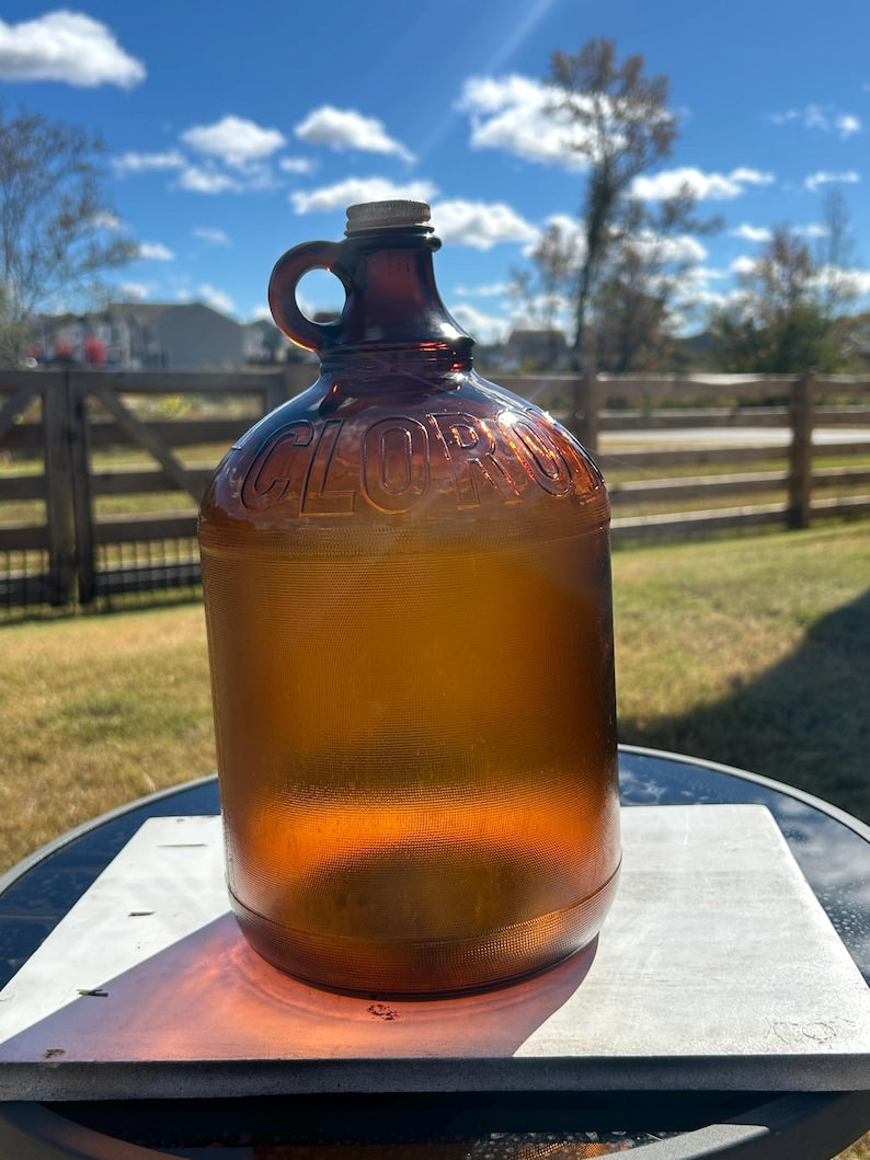 Front view of large amber glass jug with loop handle displayed outdoors.