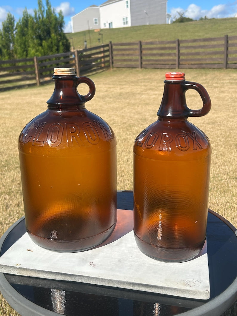 Two amber glass Clorox jugs with loop handles displayed together outdoors.