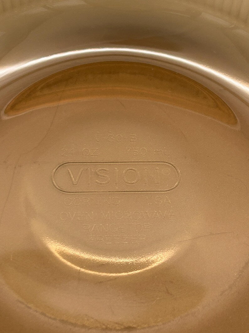 May include: A clear, round Vision brand glass bowl with a capacity of 24 oz (750 ml). The bowl is oven, microwave, range top, and freezer safe. The text "VISION" is embossed on the bowl.
