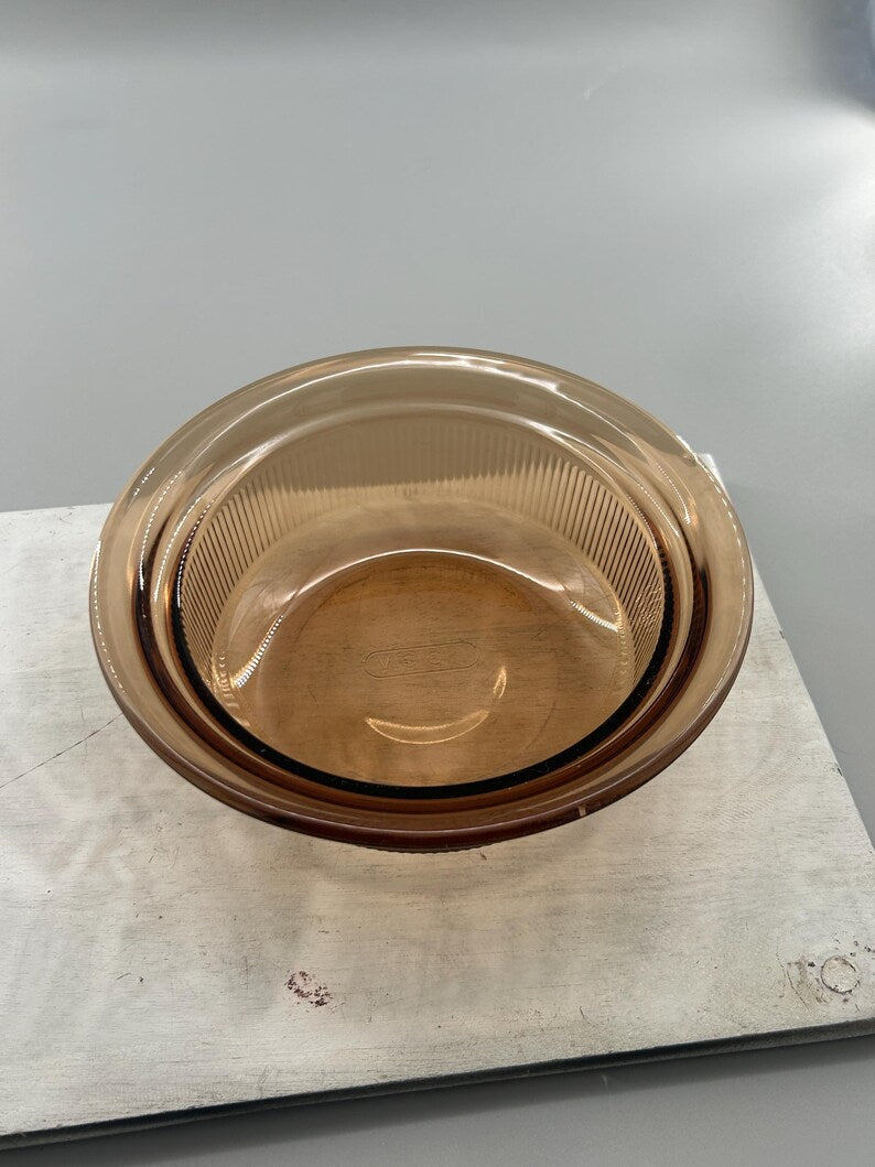 May include: A round, amber-colored glass bowl with a ribbed interior. The bowl has a smooth, rounded rim and a slightly darker band around the edge. The bowl is likely for food preparation or serving.