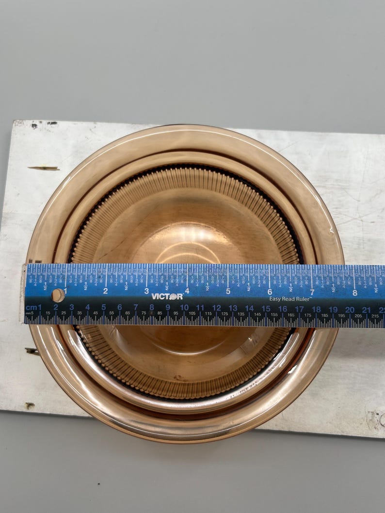 May include: A set of three nesting amber-colored glass bowls. The bowls are round with a ribbed design on the interior. A blue ruler is placed across the bowls, measuring approximately 8 inches in diameter.