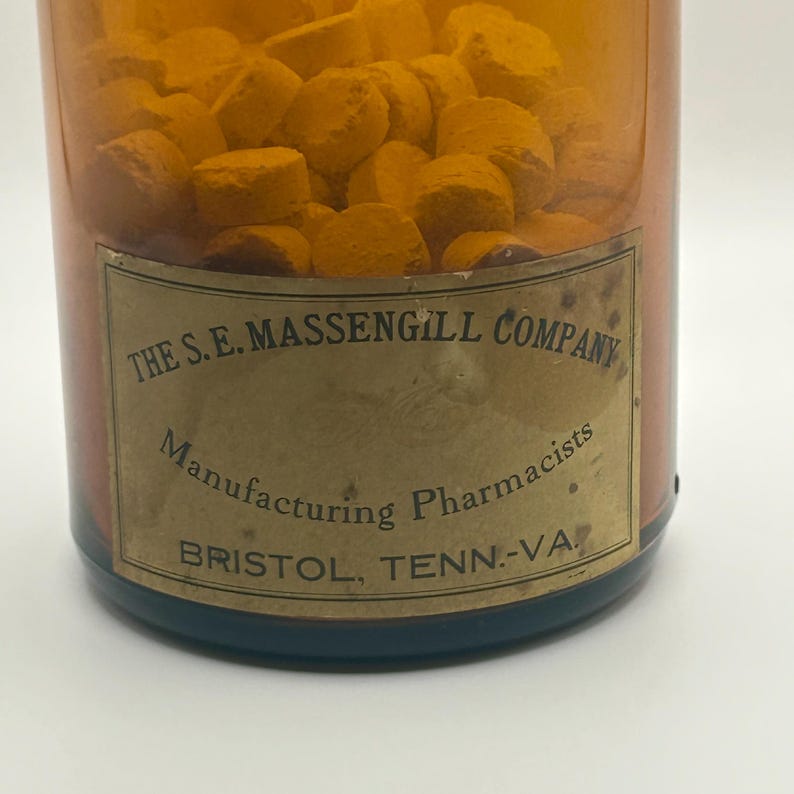 May include: A vintage amber glass bottle filled with orange tablets. The label reads "The S.E. Massengill Company, Manufacturing Pharmacists, Bristol, Tenn.-Va."