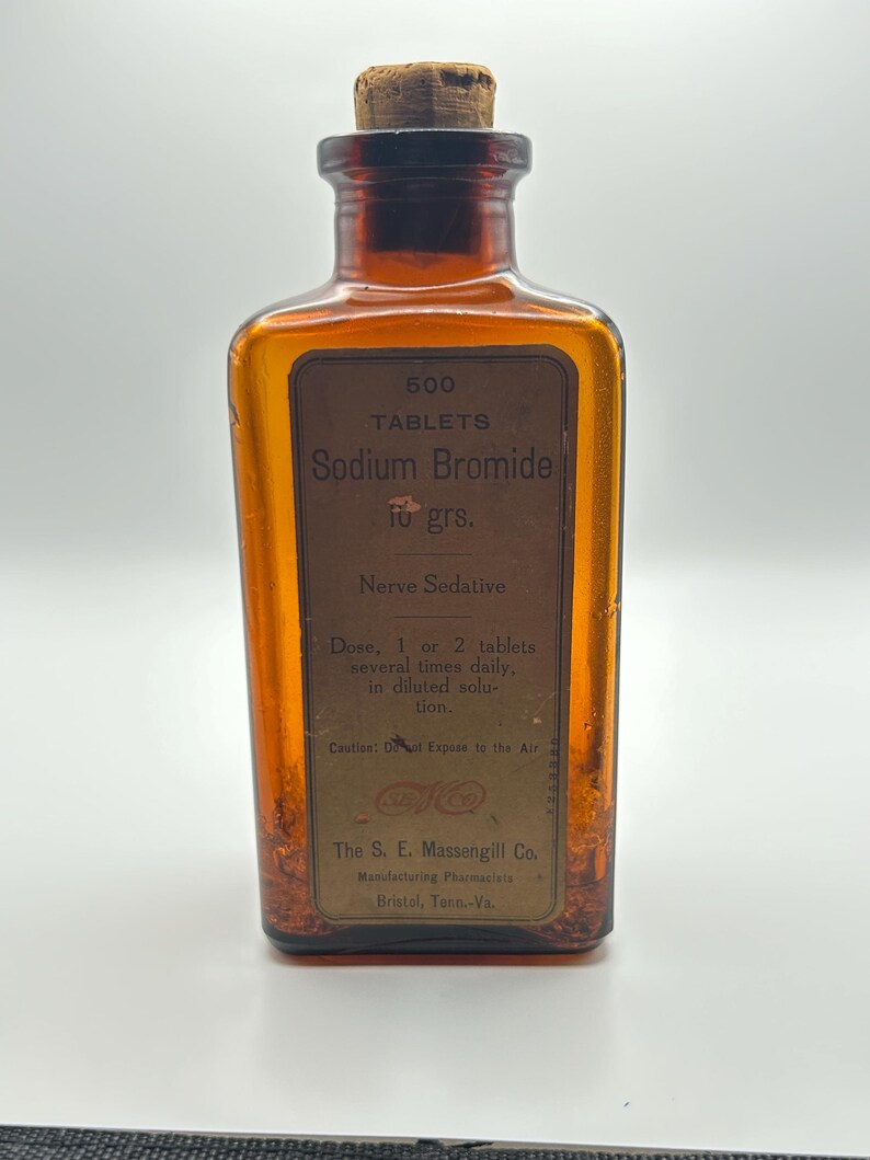 May include: An amber-colored glass bottle with a cork stopper. The label reads "500 TABLETS Sodium Bromide 10 grs. Nerve Sedative." Additional text includes dosage instructions and a warning. The bottle is from The S. E. Massengill Co.