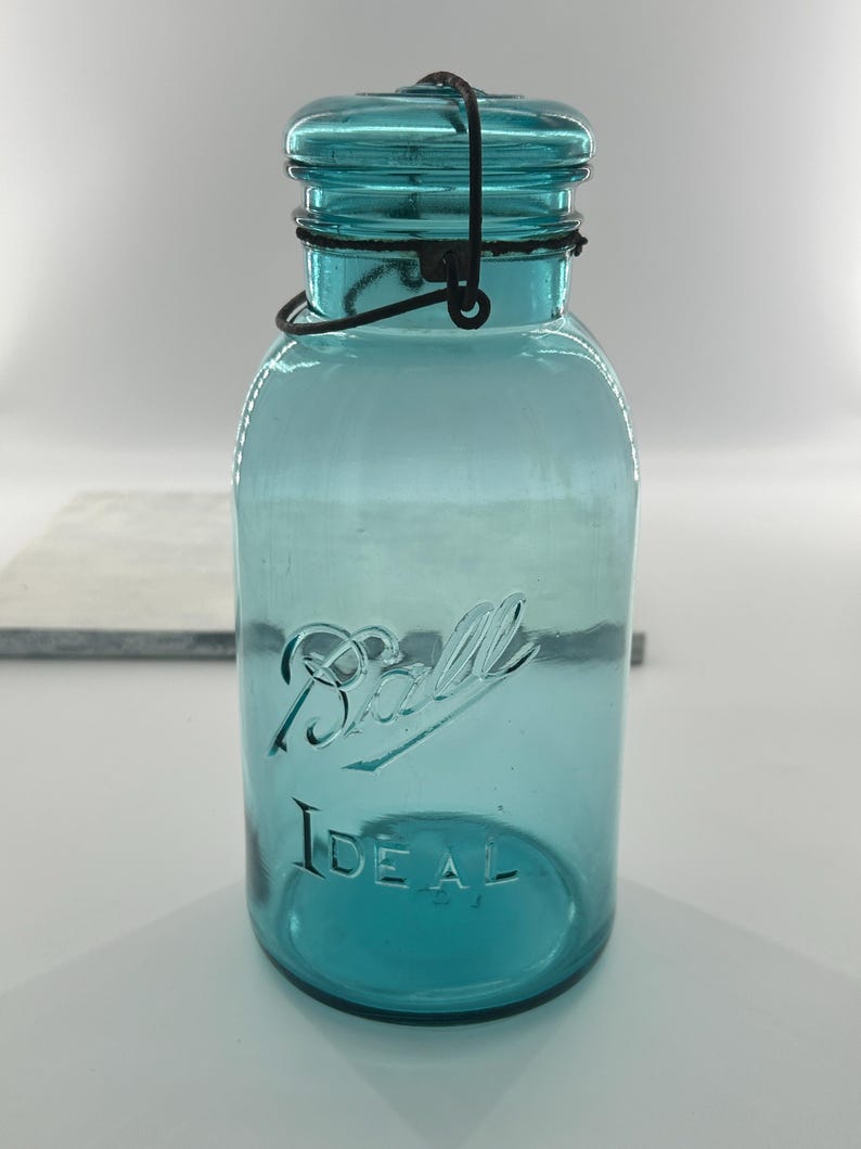May include: A vintage blue Ball Ideal jar with a wire closure. The jar has the word "Ball" in script and "Ideal" embossed on the front. The jar is made of blue glass and has a metal lid and wire closure.