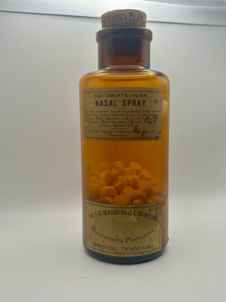 May include: An antique amber glass bottle labeled "500 TABLETS - PLAIN NASAL SPRAY" with a cork stopper. The label includes ingredient information and the text "THE S.E. MASSENGILL COMPANY, Manufacturing Pharmacists, BRISTOL, TENN-VA". The bottle is filled with yellow tablets.