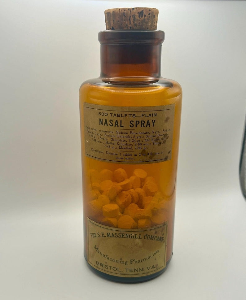 May include: An amber glass bottle with a cork stopper, labeled "500 TABLETS - PLAIN NASAL SPRAY." The bottle contains numerous yellow tablets. The label includes text about ingredients and directions, and the manufacturer's name, "THE S.E. MASSENGILL COMPANY."
