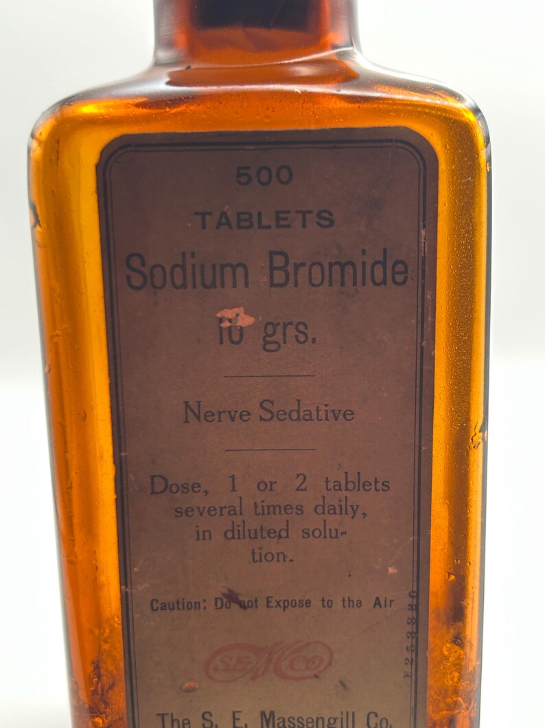 May include: An amber glass bottle with a brown label. The label reads "500 Tablets Sodium Bromide 10 grs. Nerve Sedative." The text also includes dosage instructions and a warning about air exposure.