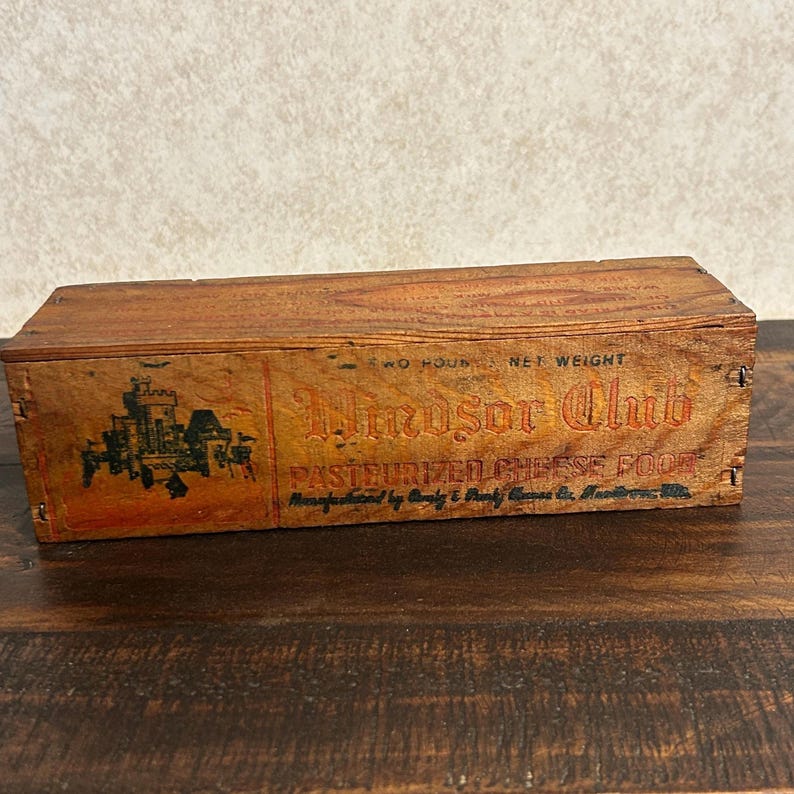 May include: Vintage wooden cheese box with the words "Windsor Club" in a decorative font. The box has a castle graphic and the text "Pasteurized Cheese Food." The box is made of wood and has a two-pound net weight.