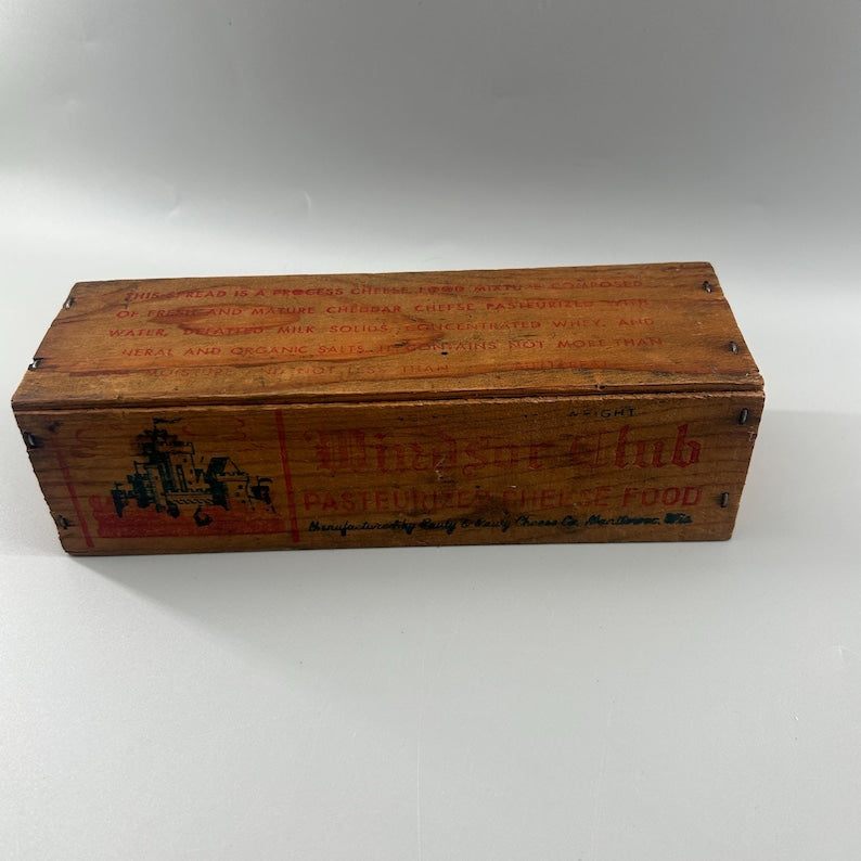 May include: A vintage wooden box with red lettering and graphics. The box is rectangular and appears to be for food storage, with text indicating it once contained cheese. The box has a weathered appearance.