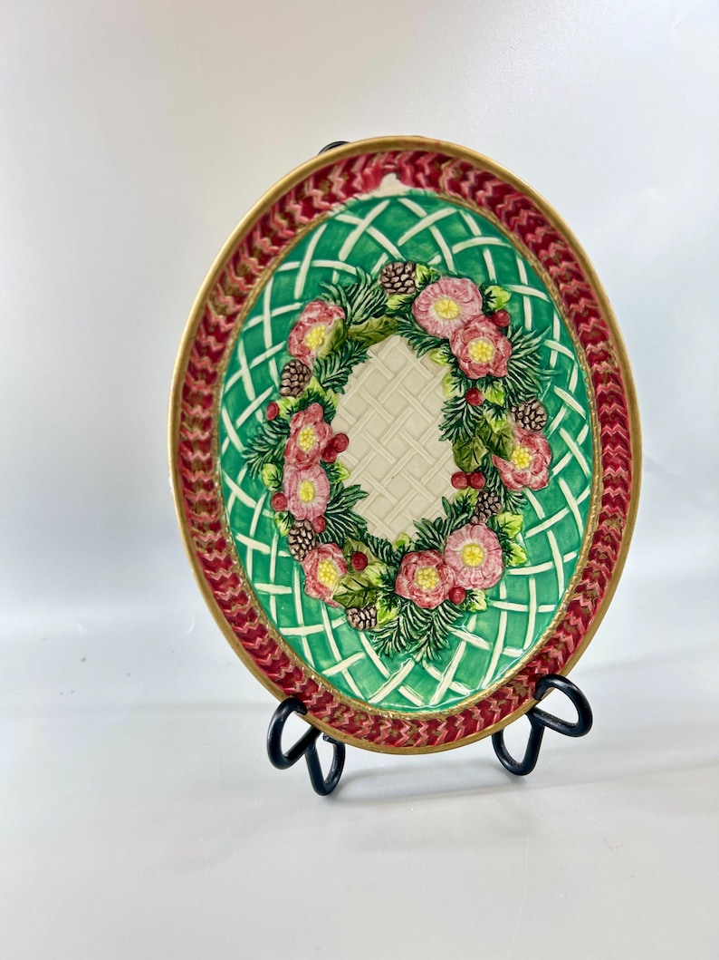 Front view of Fitz and Floyd oval serving bowl with green lattice, floral wreath, and red border.
